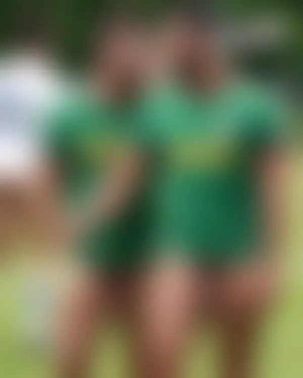 Two shirtless rugby players walking arm-in-arm across a sunlit field with playful grins and athletic tension