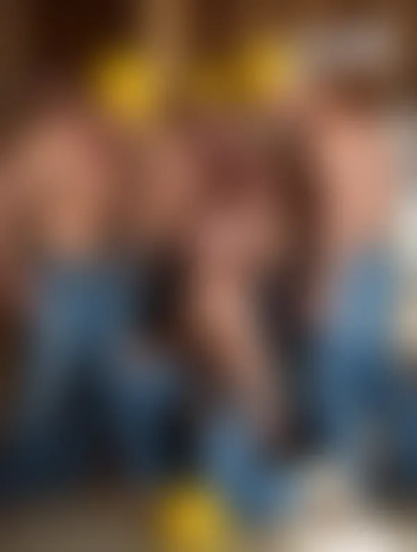 Shirtless muscular construction worker with yellow hard hat gripping a hammer beside framing lumber under bright sunligh