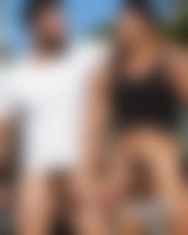 Two muscular men under bright sun, arms around each other’s shoulders, smiling warmly with relaxed intimacy in a backyar