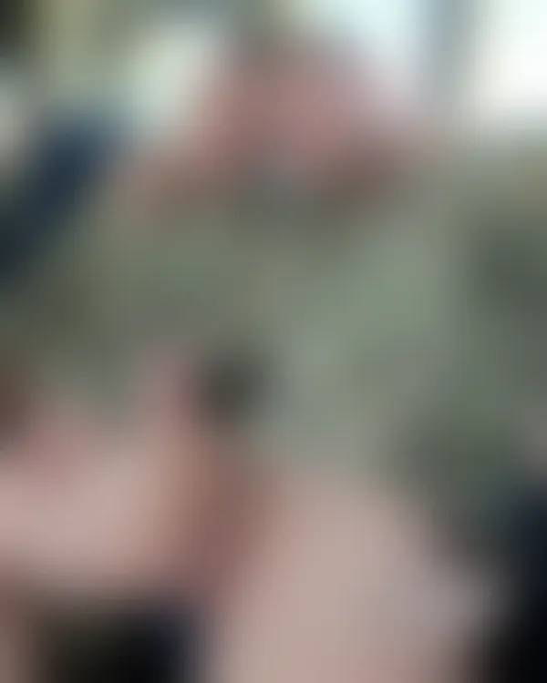 Two muscular men in military fatigues sitting close on a bus with arms around each other’s necks under warm interior lig