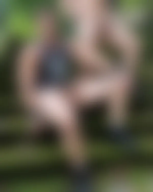 Two muscular men posing confidently on mossy forest steps with one shirtless and the other in a tank top under dappled s